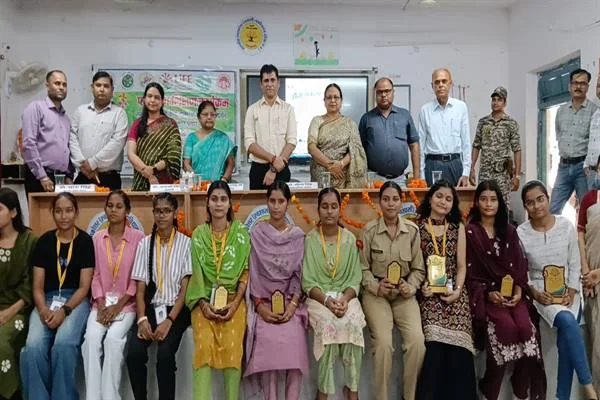 मंच पर खड़े अधिकारियों और शिक्षकों के सामने पुरस्कार लिए हुए छात्राएं समूह में बैठी हैं